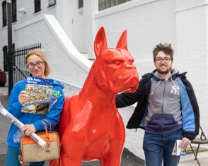 Two people pose alongside a large red sculpture of a dog