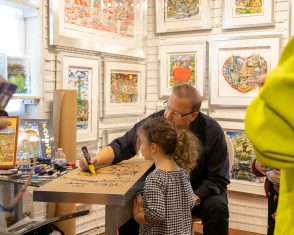 Charles drawing on a table while a young kid watches