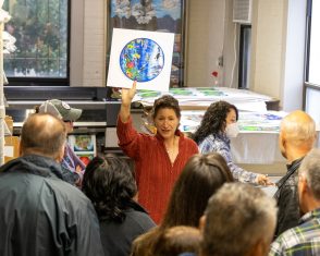 Julie holding up a print of sea of tranquility to a group of folks packed in the Fazzino studio during ArtsFest