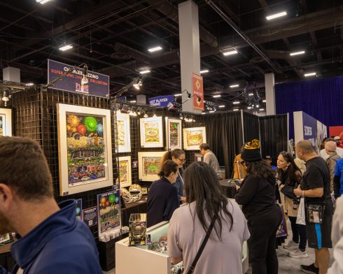 Fazzino's artwork hangs on the wall behind folks looking at helmets and other hand-painted artwork for the Super Bowl 