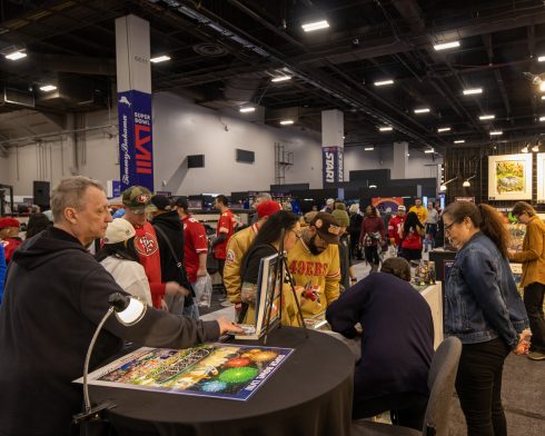 Fazzino signing posters at the Super Bowl LVIII booth at the NFL experience which is packed with people