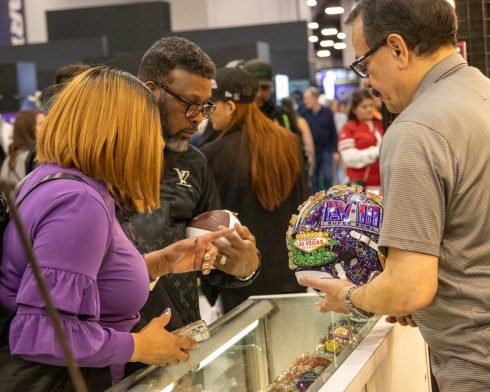 A man shows a women a close-up of the hand-painted helmets Fazzino creates for Super Bowl LVIII