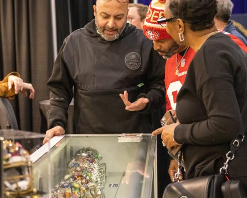 Two people look at the case showing hand-painted helmets for Super Bowl LVIII