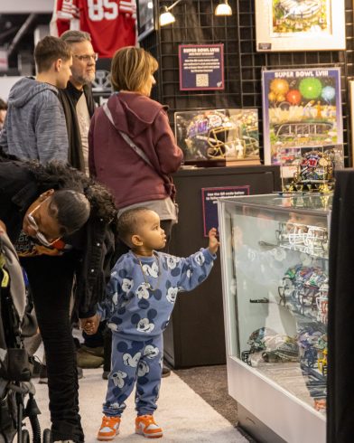 A young kid looks at a case of hand-painted helmets for Super Bowl LVIII