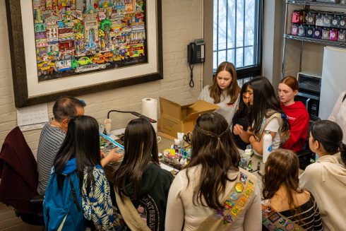 A group of Girl Scout students stand around a table at the Fazzino studio to look at how the artwork gets created