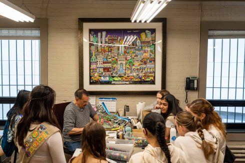 A group of Girl Scouts gather around a table at the Fazzino studio to watch how the artwork is cut and constructed