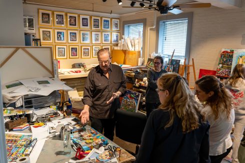 A Girl Scout troop gathers around a table at the studio with Fazzino pointing the aspects of his art process